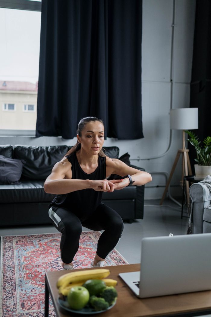 Adult woman performing squats during an online exercise session in her living room.